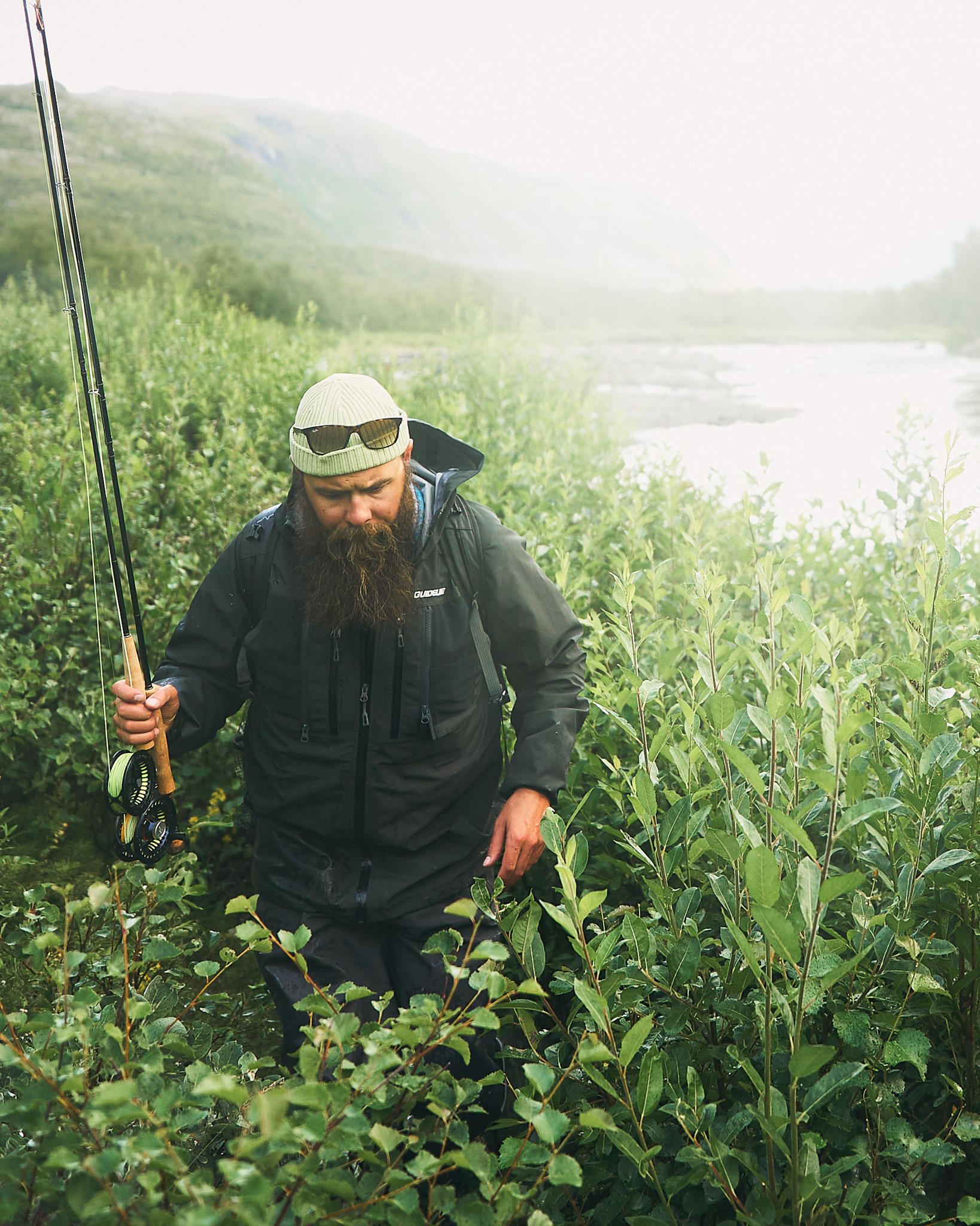 Fly fisherman walks along a foggy river with his fly rods in hand.