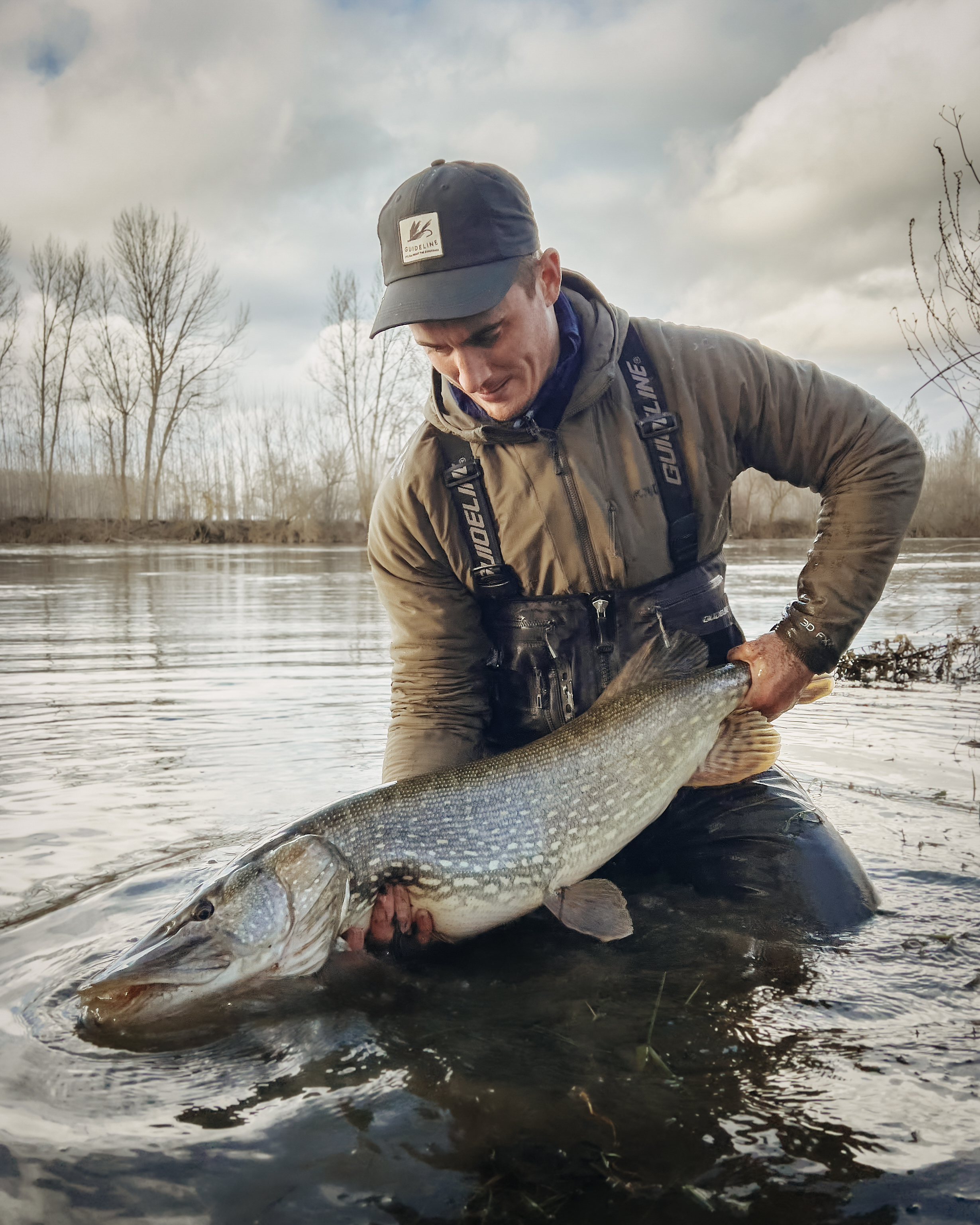 Fly angler in a river holding a big pike.
