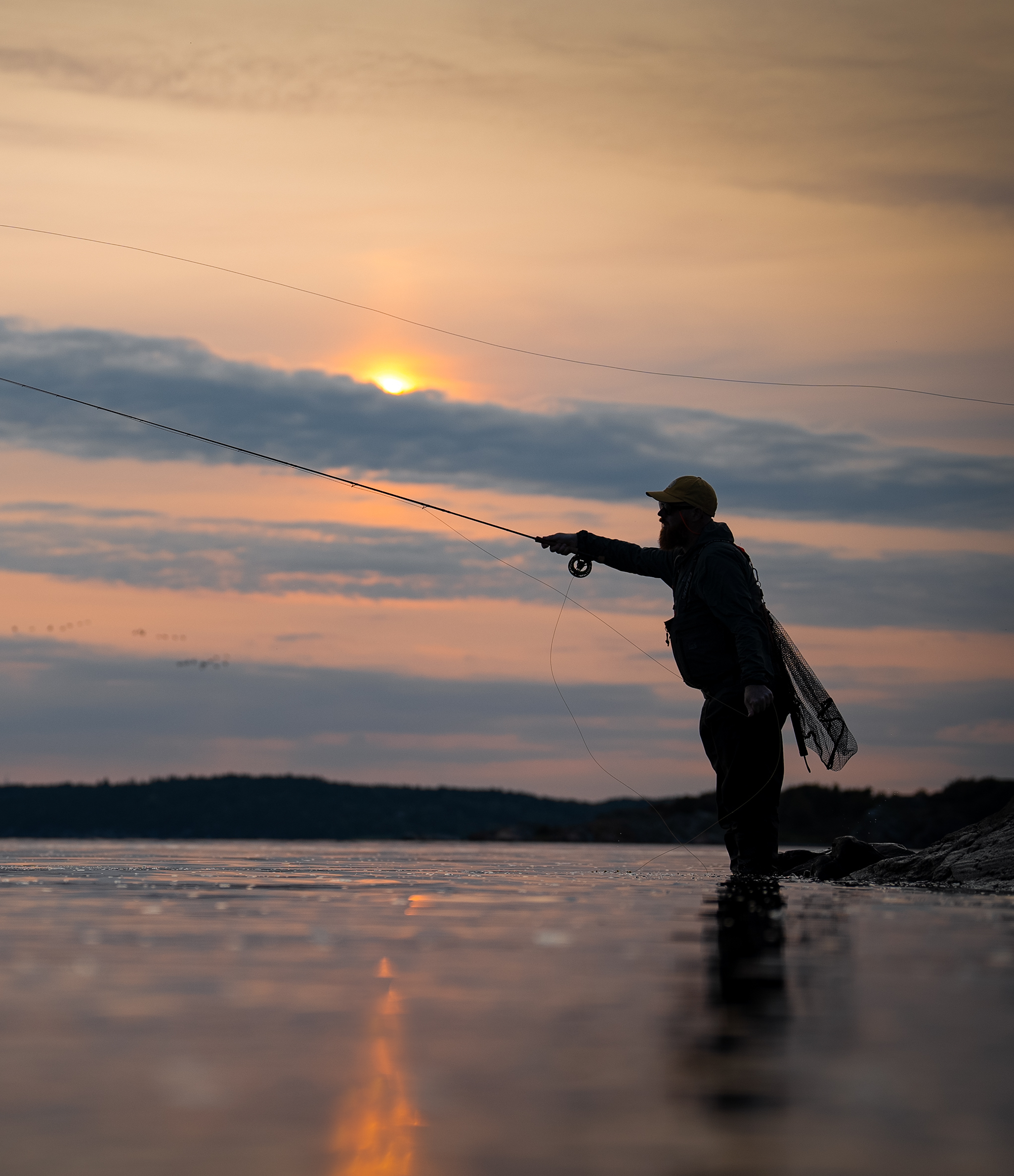 Fly angler on the coast casting a fly rod in the sunset.